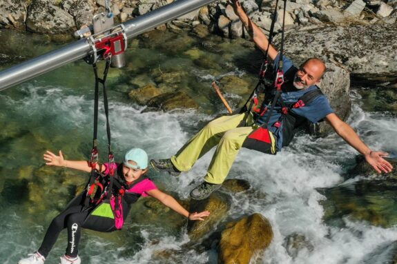 Two riders on a zip line (Flying Fox) over a rocky river, safely speed-limited by an Amsbeck centrifugal brake.
